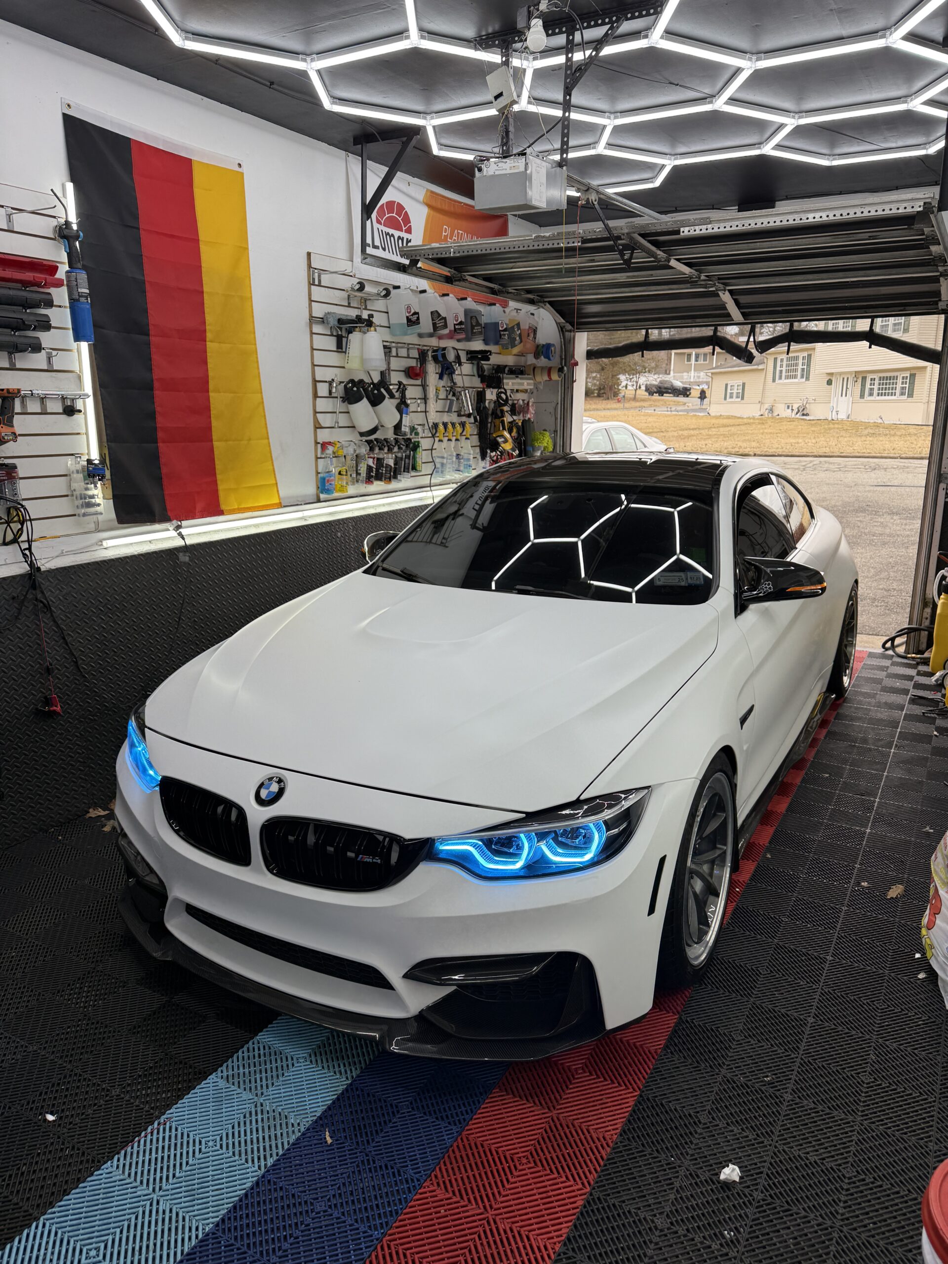 White BMW M4 with blue headlights and ceramic coating in detailing bay